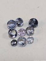 Photo of nine loose tanzanite gemstones in various sizes and oval and round cuts on a white background.
