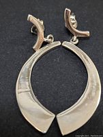 Top view of the pair of silver earrings laid on a black background showing their crescent shaped design and post backs.