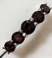 Close-up image of a silver ring set with five deep red garnet gemstones, showing the facets and prong settings clearly.