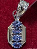 Front close-up of silver pendant showing four vertically aligned marquise tanzanite stones in prong settings against red background.