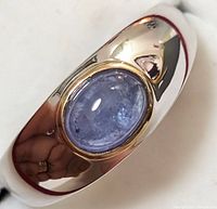 Close-up of polished sterling silver ring showing oval cabochon tanzanite in gold-tone bezel setting, reflective smooth band, size 10.5