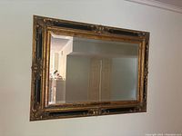 Full view of the large rectangular mirror hanging on a wall, showing the carved black and gold frame and the reflected room.