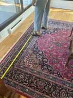 Persian rug laid flat on hardwood floor with measuring tape showing width measurement of 96 inches.