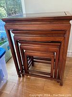 Four wood nesting tables nested together, largest with glass top visible