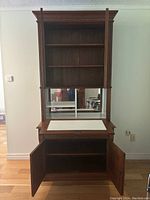 Front view of vintage solid wood cocktail cabinet showing upper open shelves with mirrored back, middle countertop, and lower open cabinet with doors.