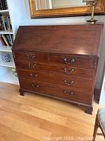 Wooden vintage secretary desk closed showing drop-front panel, three drawers with brass handles, decorative bracketed feet.