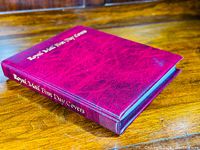 Red hardcover album angled on wooden surface showing embossed text "Royal Mail First Day Covers" on spine and front cover.