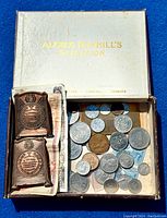Dunhill box containing vintage coins, bronze medals, and paper currency visible inside the box.