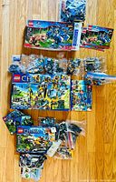 Overview of four LEGO sets and loose pieces on floor, including Jurassic World box, Speed Champions box, two Chima boxes, and numbered bags