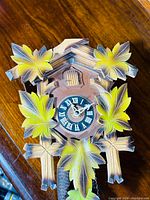 Front view of the carved wooden cuckoo clock showing painted leaves and clock face with Roman numerals.