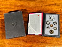 Image showing the black presentation case with 7 coins arranged in foam insert and a certificate card inside the case.