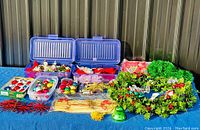 Overview of the lot showing opened blue plastic boxes containing small glass ornaments, a partially visible wreath, tinsel garland and other assorted decorations on a blue surface.