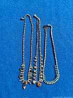 Three vintage rhinestone necklaces with colored stones laid out on blue fabric, showing entire length and design.