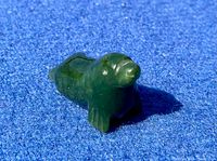 Front perspective view of the small dark green jade seal carving on a blue background showing the seal's head, flippers, and body shape.