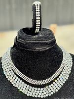 Two rhinestone choker necklaces displayed on a black necklace stand, showing the sparkling clear rhinestones in multiple rows close up.