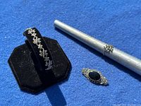 Photo of bracelet on black display stand, ring on ring mandrel, and bar brooch placed together for size comparison and style matching.