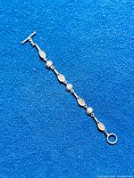 Full view of the tennis racket and ball link sterling silver bracelet laid on blue background.