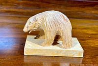 Side view of carved wooden bear showing texture and form on wooden base