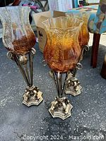 Three amber glass candle holders with ornate metal bases, shown grouped together.