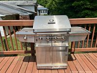 Closed hood view of stainless steel grill on deck showing front profile, side shelves and cabinet doors.
