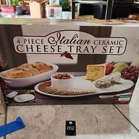 Photo of the box front showing the 4 piece Italian ceramic cheese tray set with images of the tray, bowl, and spreader alongside bread and cheese.