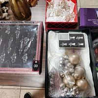 Top view of the lot showing all ornament sets including the boxed glass drop ornaments, the boxed small clear bells, and the plastic bag with metallic baubles.