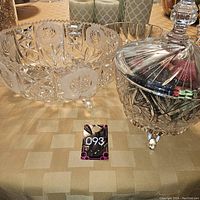 Pair of two crystal bowls seen on a table, one large bowl with etched rose and star designs, and one covered candy dish with lid and knob, both clear crystal.