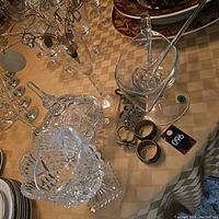 Crystal decor lot with various crystal bowls, covered jar, glasses, and napkin rings arranged on a patterned tablecloth