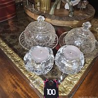 Top-down and angled views of two crystal butter dishes with lids and two glass candle holders holding violet candles on a table surface.