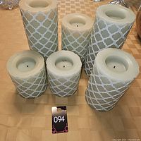 Top and side view of six flameless pillar candles showing their white lattice design and size variety.