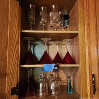 Red martini glasses and frosted blue martini glass with blue stem and base on a wooden shelf