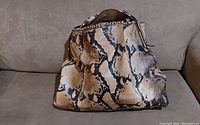 Front view of slouchy hobo purse with python print leather and braided trim around opening, placed on beige couch.