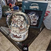 Photo of the Johnson Bros Friendly Village holiday snow globe and its original box placed on a glass table.