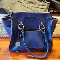 Front view of bluish purple London Fog purse showing gold-tone hardware details on the handles and front zipper pocket.