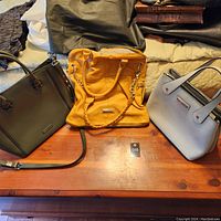 Three purses laid out on a wooden table, one mustary yellow Steve Madden purse, one green structured Steve Madden purse, and one light gray purse (not included as per description).