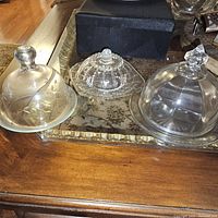 Three round glass butter dishes on wooden table; each with unique glass lid and base designs.