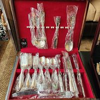 Full view of open wooden box displaying a stainless steel silver dining flatware set with ornate handles, pieces wrapped in plastic