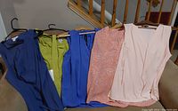 Five sleeveless tops hung on hangers with various colors and styles including navy blue, green, bright blue, patterned orange, and light pink.
