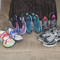 Photo of five pairs of sneakers of various colors and styles on a beige couch showing overall condition and appearance.