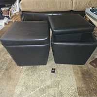Two black faux leather storage cubes side by side on carpet; one with lid closed and one with lid removed showing storage capacity.