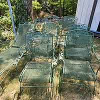 Green painted wrought iron patio chairs and chaise lounges arranged on grass.