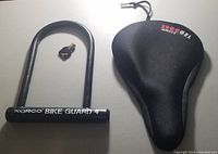 Norco Bike Guard 4 bike lock with its black key and black Ergo Gel bike seat cushion cover photographed together on a table.