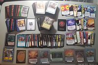 Top-down view of over 400 assorted collectible cards laid out, including Magic the Gathering, VS System Marvel, Chaotic, and Digimon cards. Cards appear in multiple piles, some boxed or sleeved.