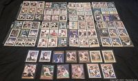 Top-down view of approximately 70 baseball cards arranged in rows on a black surface.
