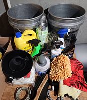 Full lot display showing two black buckets, various spray bottles, microfiber mitt and towels, brushes, rope, and accessories on wooden surface.