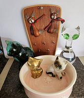 Photo showing entire cat lot including glass cat figure, brass and ceramic cats, wooden cat key hanger, and pet water bowl with figurines inside.