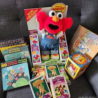 Overview of assorted children's toys including vinyl records, Elmo plush in box, Disney collectibles, and children's toys.