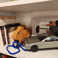 Photo of wooden rabbit pull toy beside silver VHS rewind car toy and a notebook.
