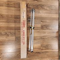 Folded vintage aluminum artist easel placed on wooden floor with original Starnite branded box alongside it.