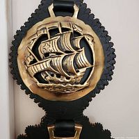 Close up of top horse brass with detailed sailing ship mounted on scalloped black leather
